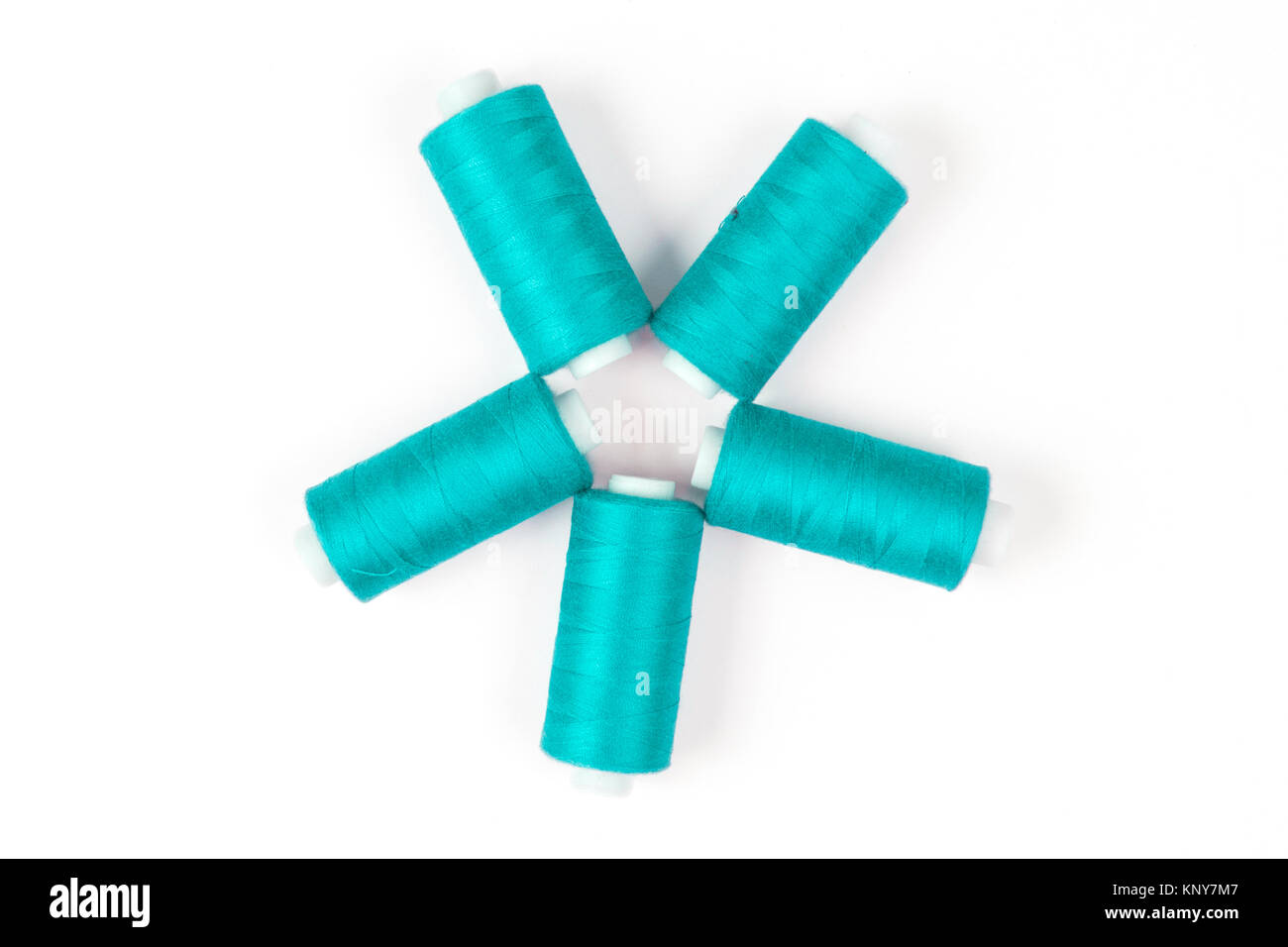 Five turquoise sewing threads laying in a circle on a white background, sewing accessories Stock Photo
