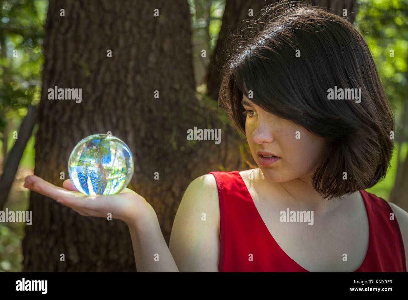 Young woman, standing by a tree in a park, holding a crystal ball. Stock Photo
