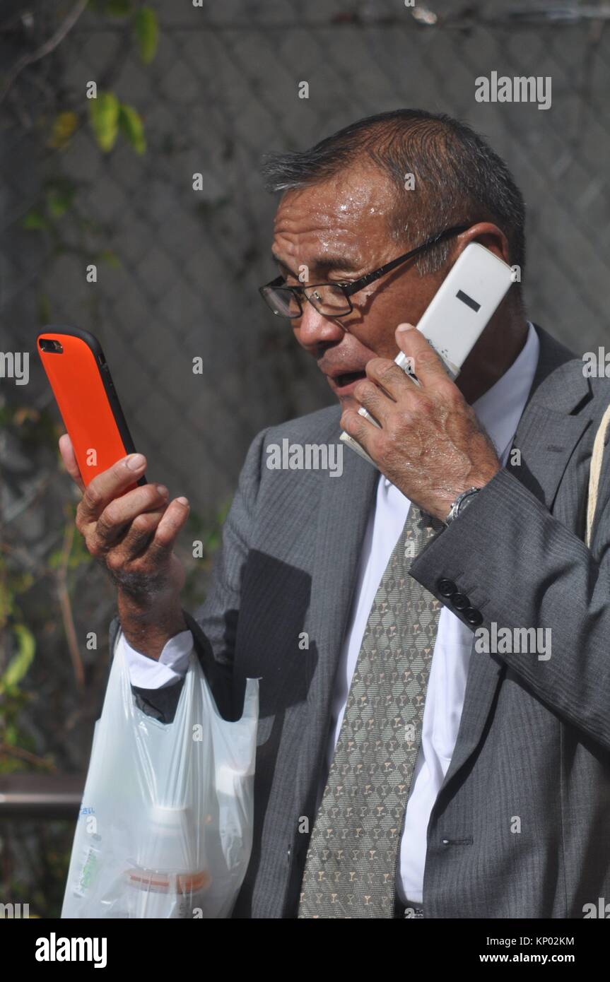 Naha, Okinawa, Japan: a man using two mobile phones at the same time Stock Photo