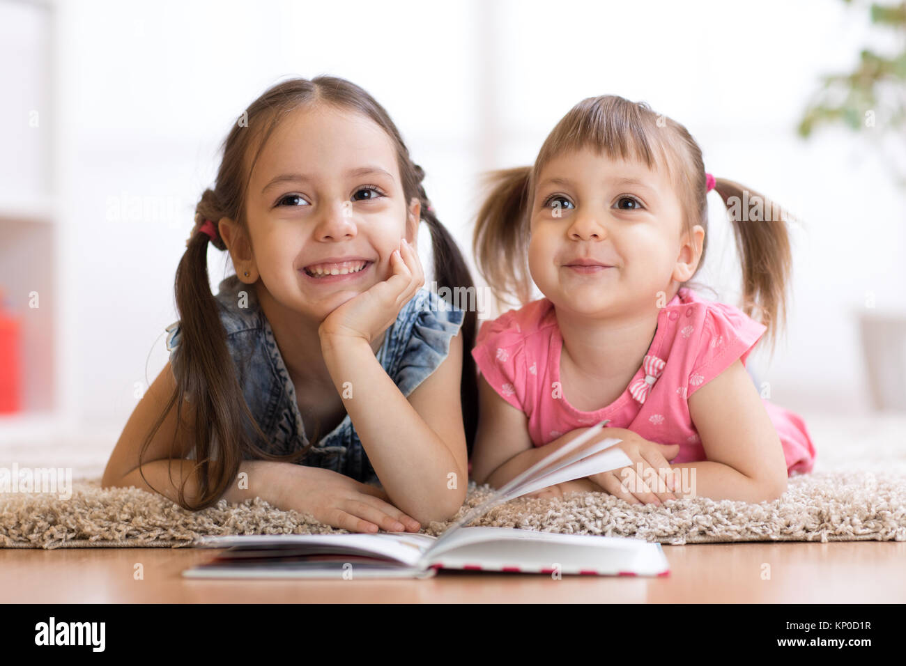 Two children lying on floor and reading book Stock Photo