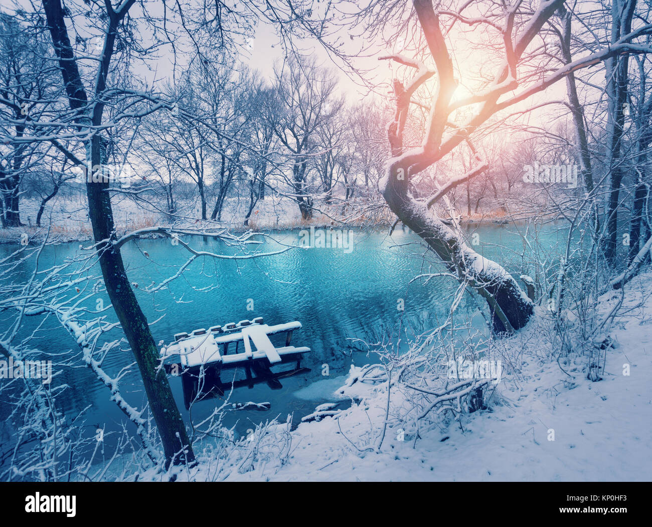 Winter forest on the river at sunset. Colorful landscape with snowy trees, river with reflection in water in cold evening. Snow covered trees, lake, s Stock Photo