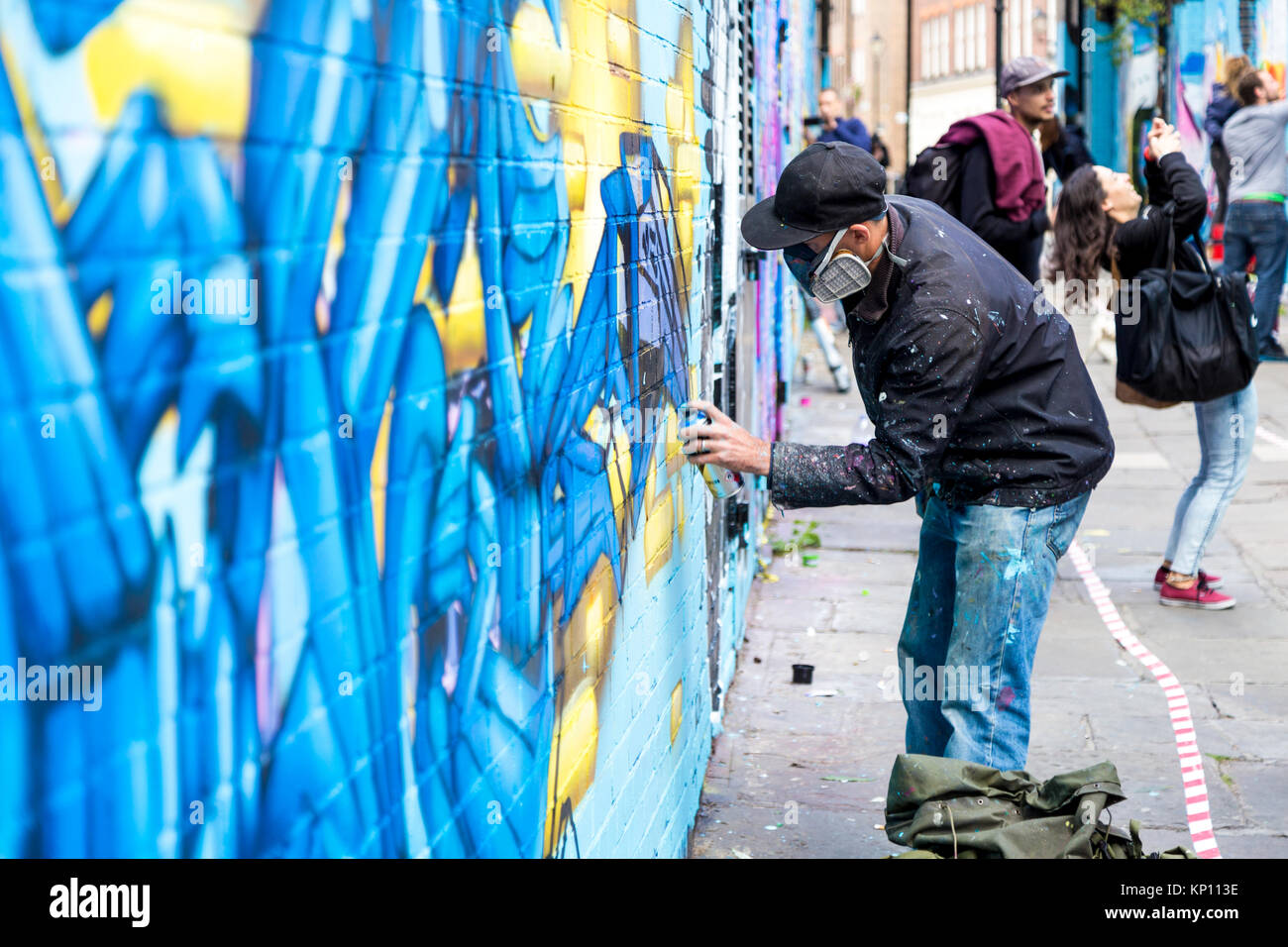 Graffiti street artist wearing a respirator mask spraying the walls in Fleur Street, London, UK Stock Photo