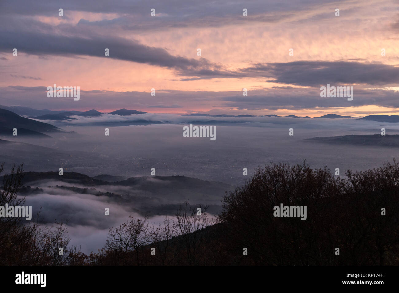 Umbria valley in winter filled by mist at sunset, with emerging hills, hidden Foligno city lights  and beautiful warm, purple and orange tones Stock Photo
