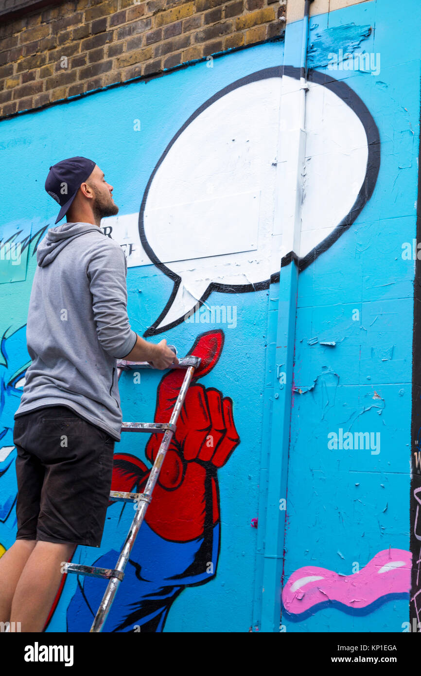 Graffiti street artist spraying the walls in Fleur Street, London, UK Stock Photo