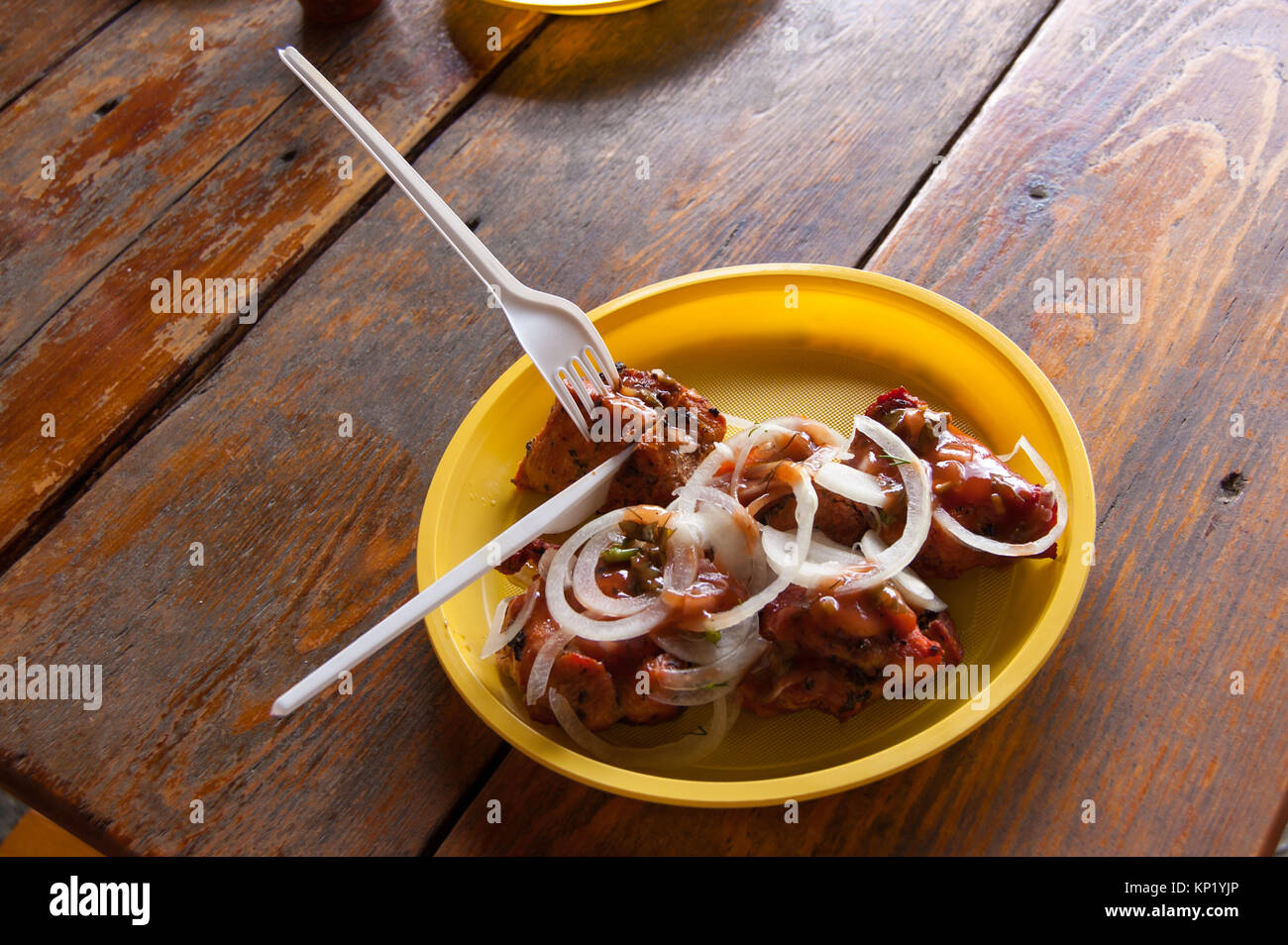 pieces of fried meat with pieces of onions on a yellow plastic plate Stock Photo