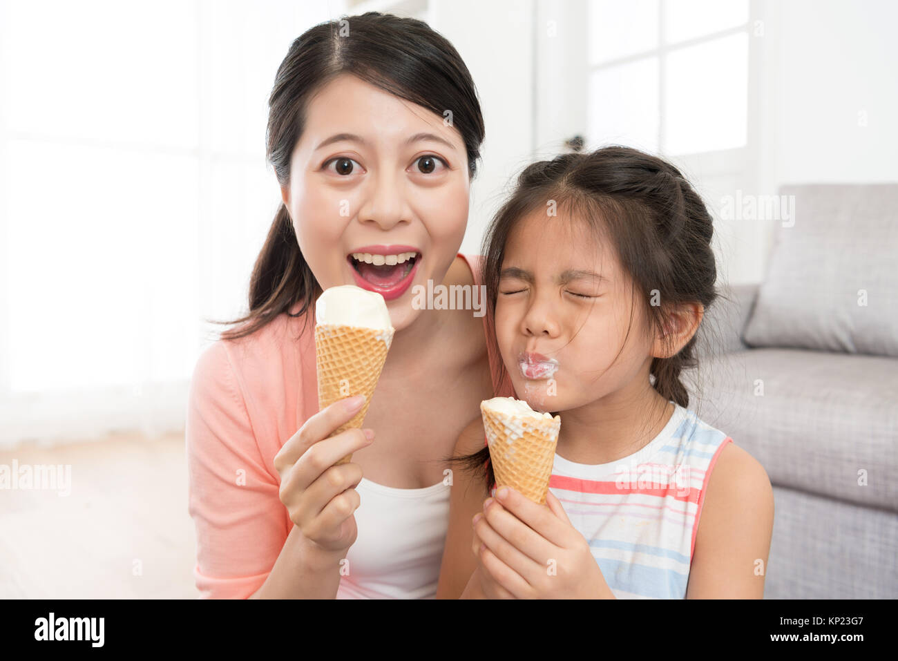 happy pretty woman holding dessert looking at camera laughing and cute little kid children girl enjoying eating ice cream. Stock Photo