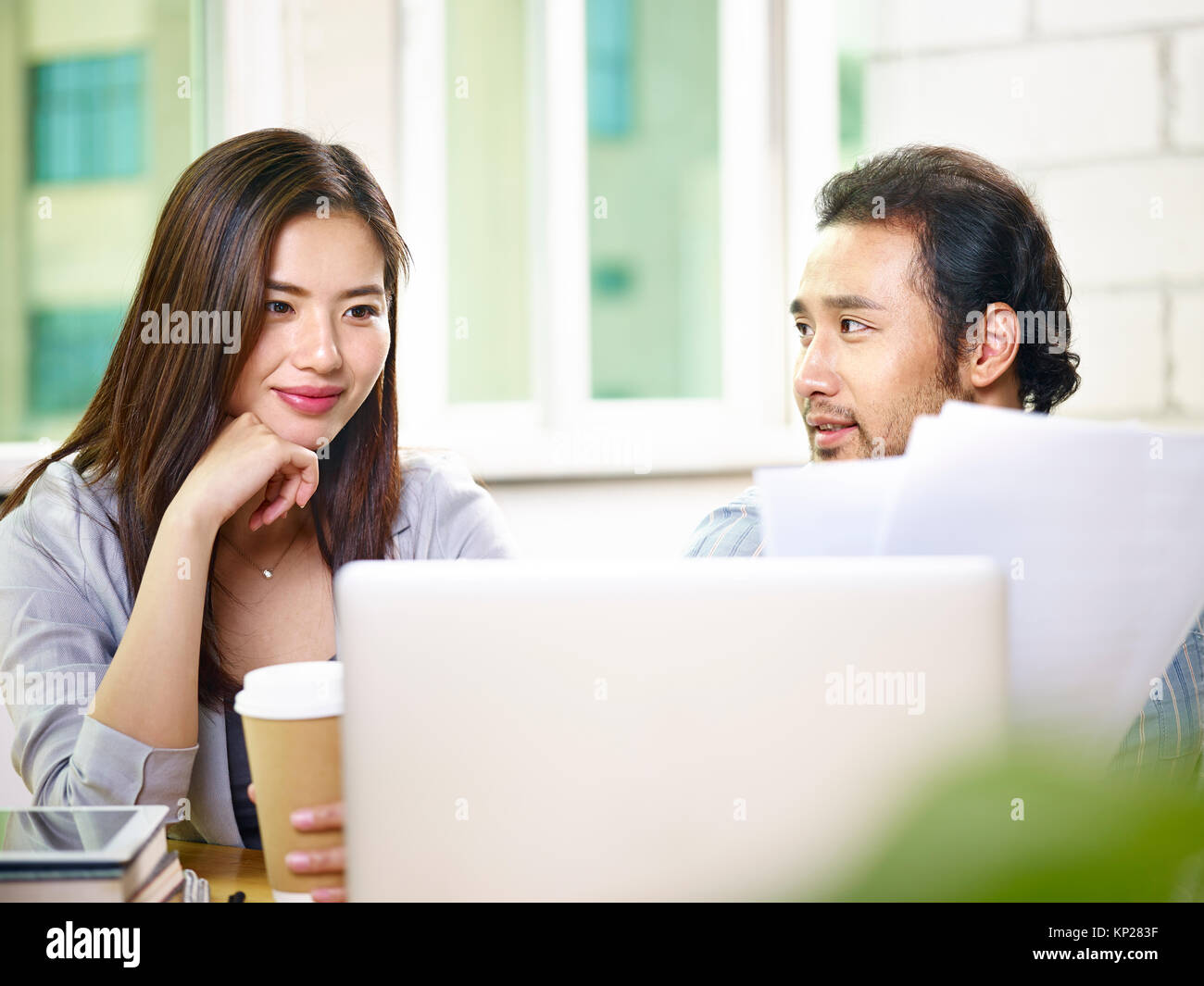 two young asian business colleagues coworkers teammates working together in office analyzing report using laptop computer. Stock Photo