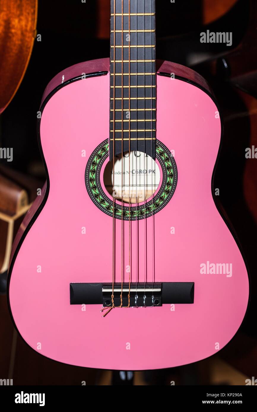 pink coloured spanish guitar for sale hanging in a music shop Stock Photo