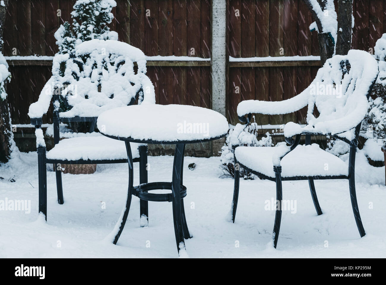 Black metal garden furniture in a garden in winter, covered in snow