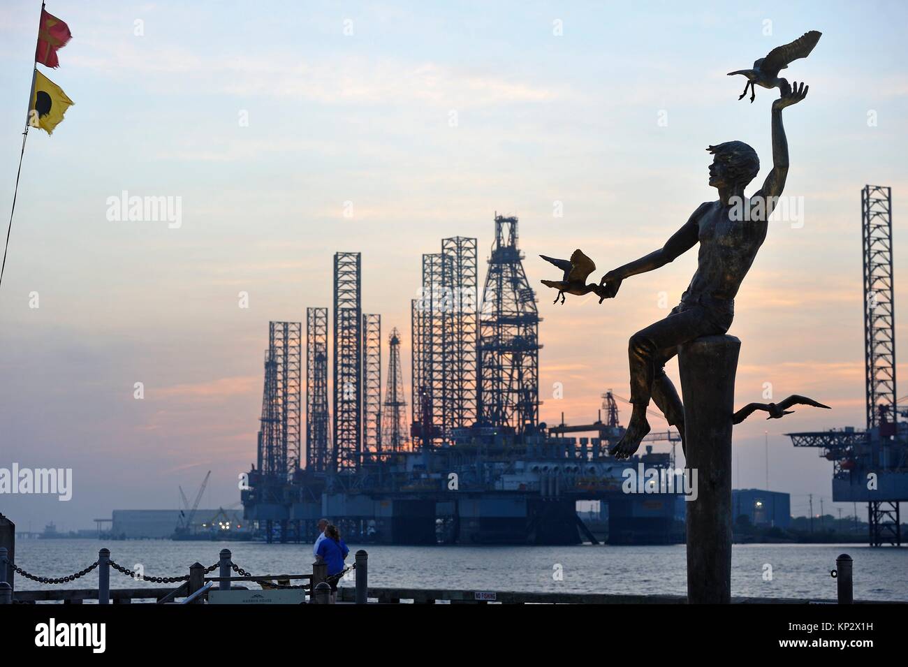 ´´High Tide´´ bronze statue by Charles Parks with oil platform in the background at sunset, Port of Galveston, Galveston island, Gulf of Mexico, Stock Photo