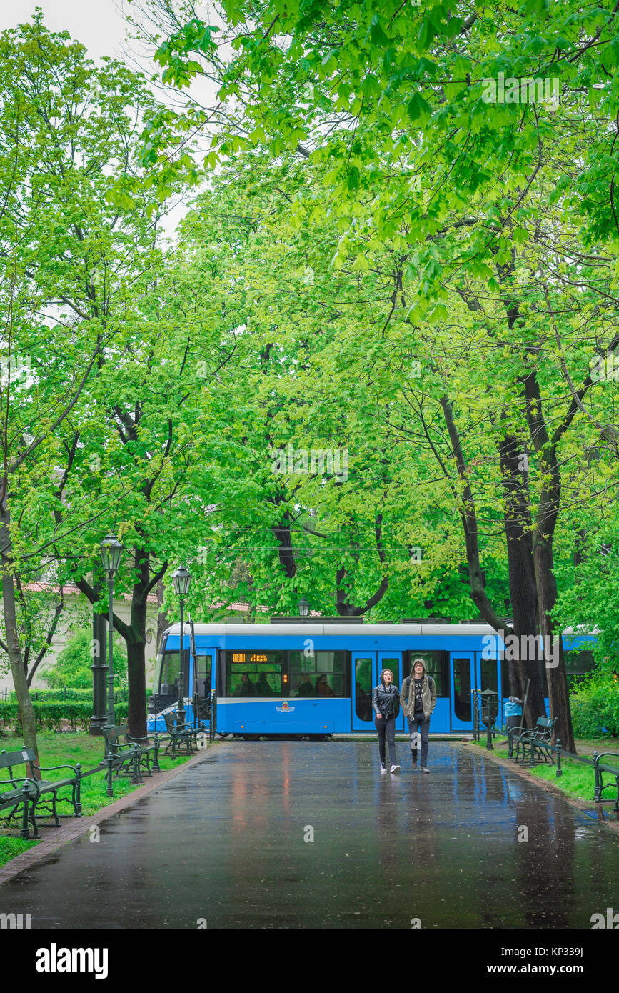 Couple walking rain, under a late spring shower of rain a young couple walk through Planty Park in Krakow, Poland. Stock Photo
