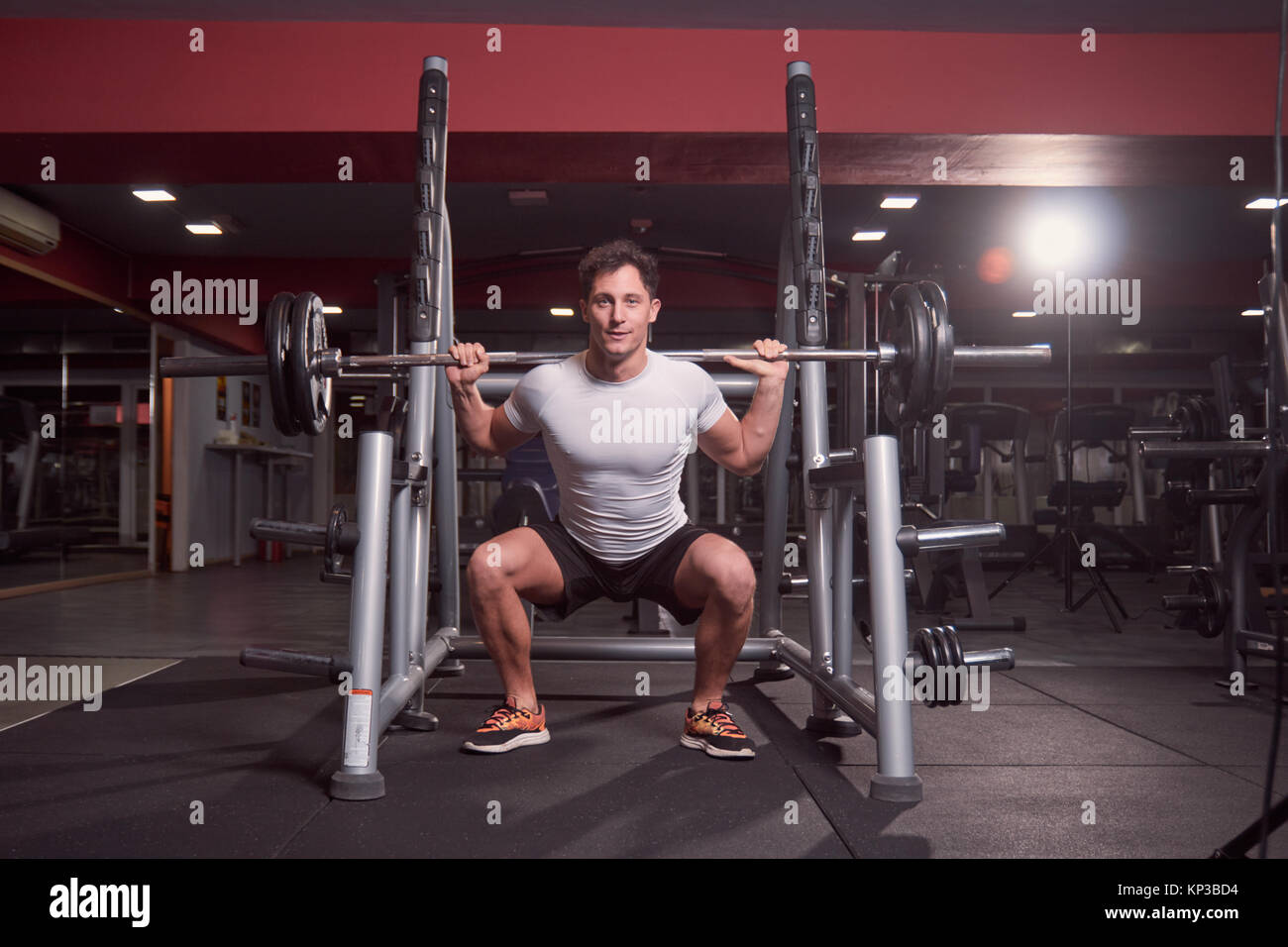 one young man, barbell back squat, dark gym indoor. full lenght body shot. Stock Photo