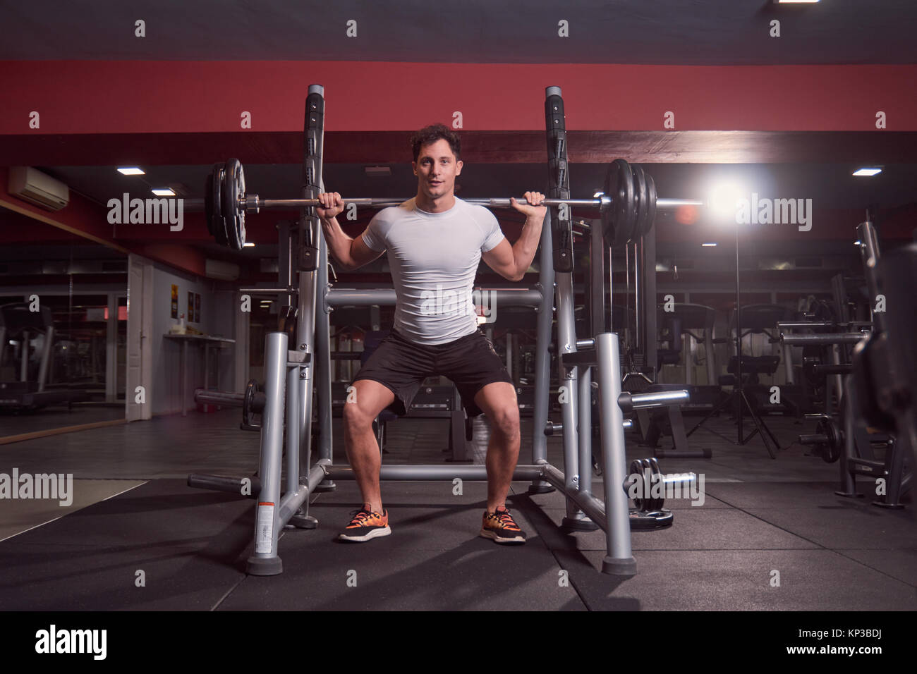 one young man, barbell back squat, dark gym indoor. full lenght body shot. Stock Photo