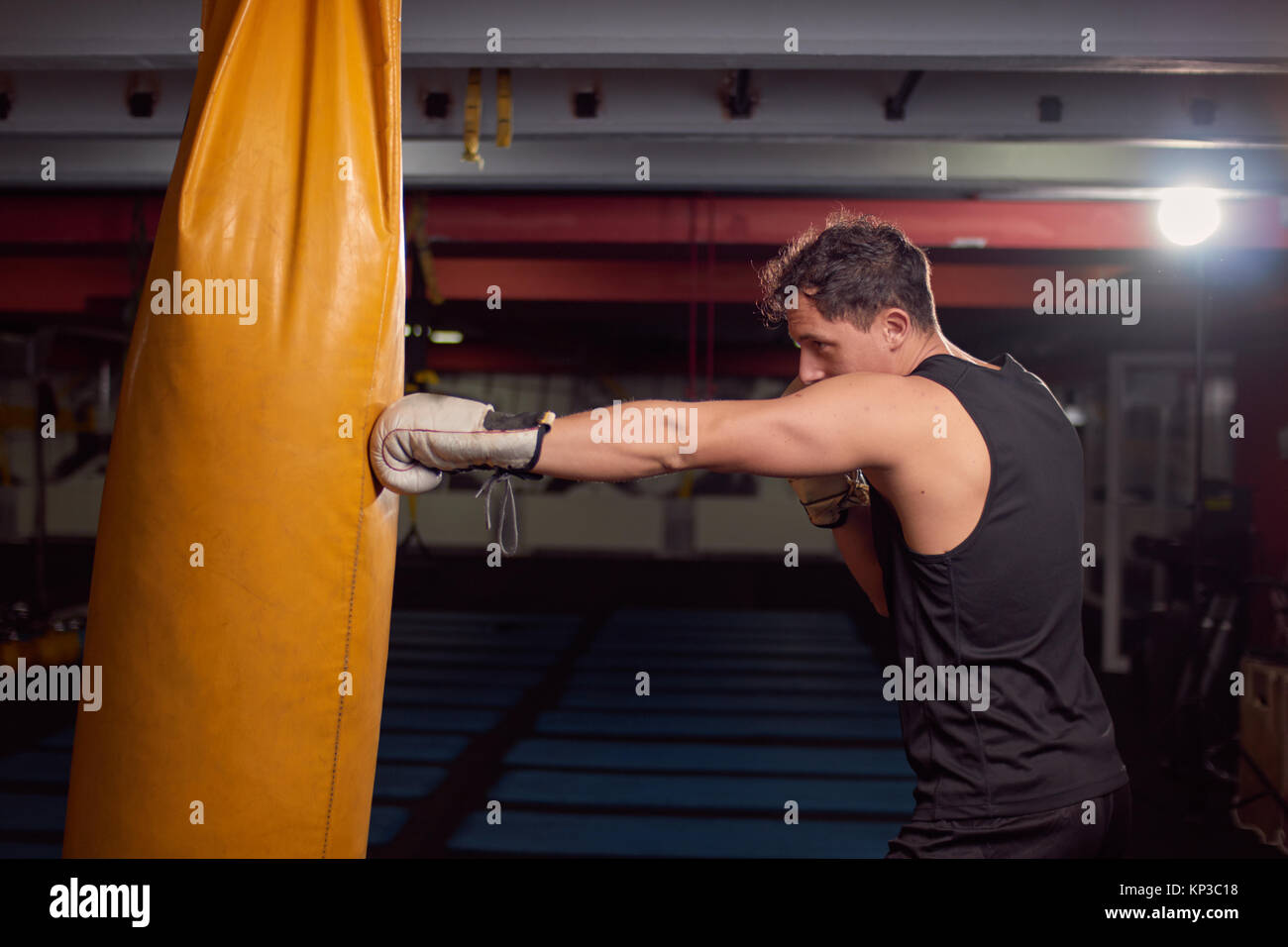 one young man, boxer hand hitting punching bag, practicing indoors gym room, wearing boxing gloves, upper body shot. Stock Photo