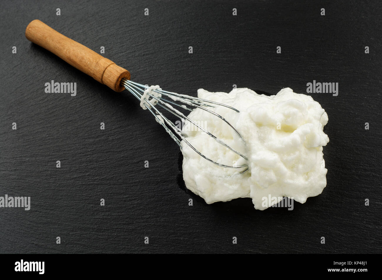 Process of cooking meringue. Whipped egg whites on whisk on slate
