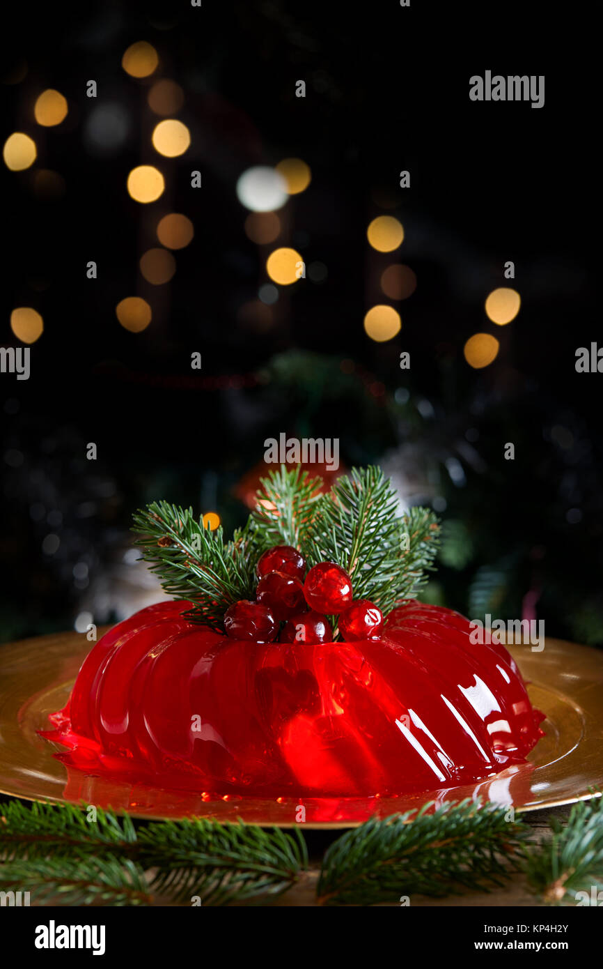 Red jelly decorated for Christmas with fir branches and candied cherries, on dark background with bokeh lights. Stock Photo