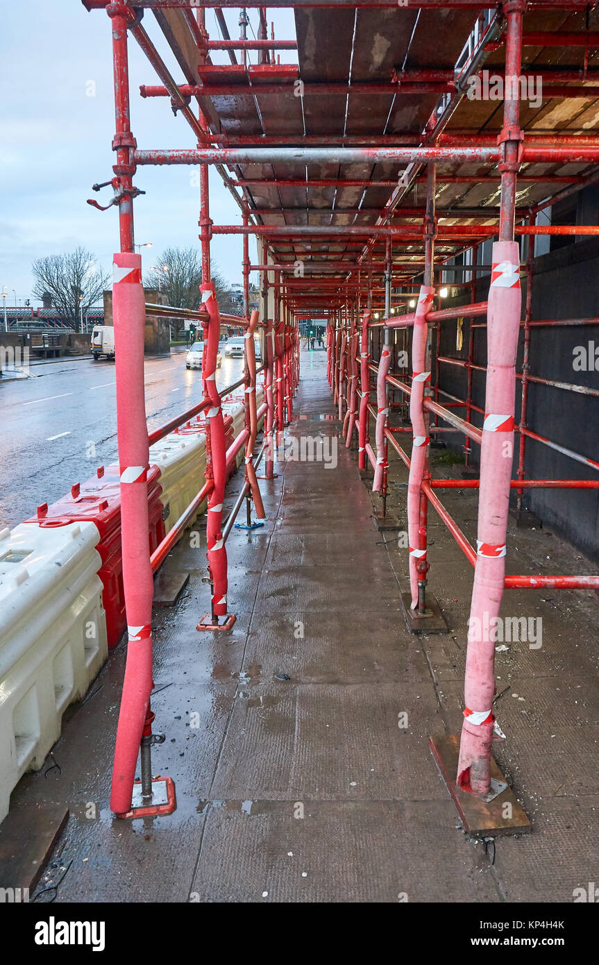 Safe passage for pedestrians made out of red scaffolding on a typical construction site in UK. Stock Photo