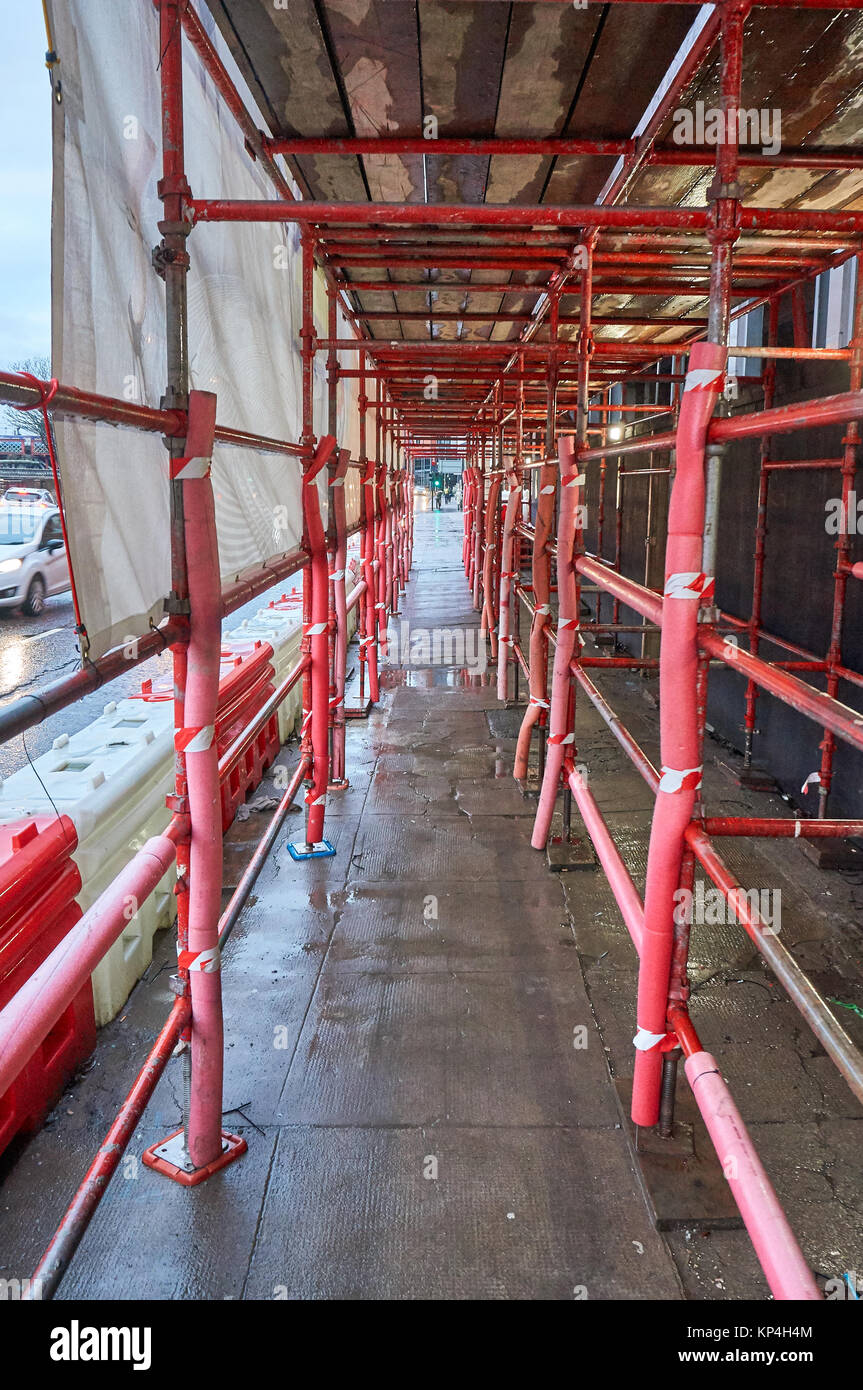 Safe passage for pedestrians made out of red scaffolding on a typical construction site in UK. Stock Photo