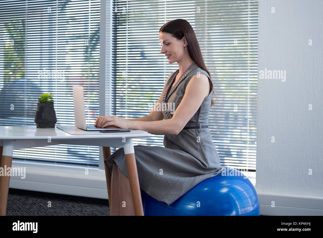 Female Executive Sitting On Exercise Ball While Using Laptop At