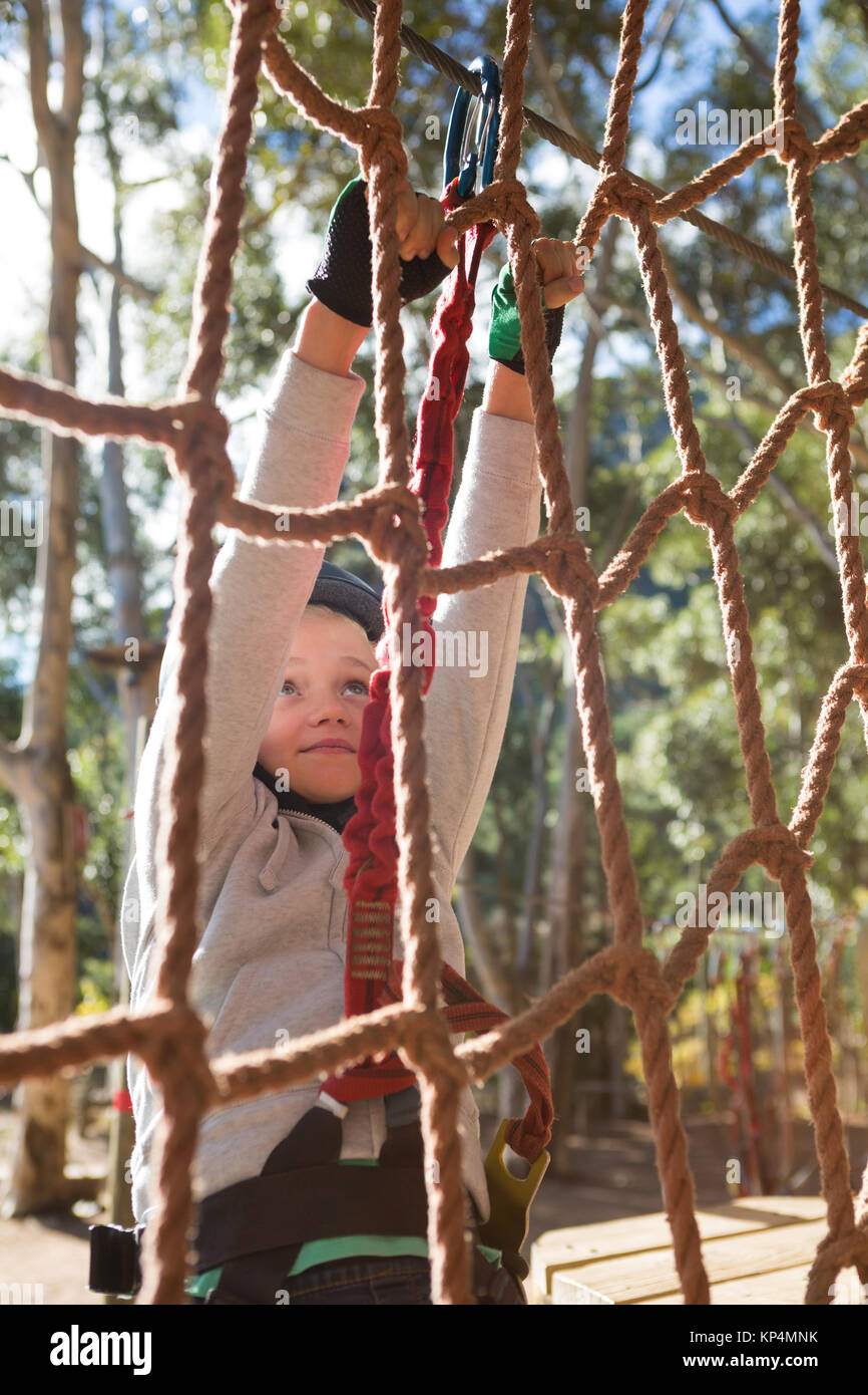 Little girl wearing safety harness climbing rope fence in the forest