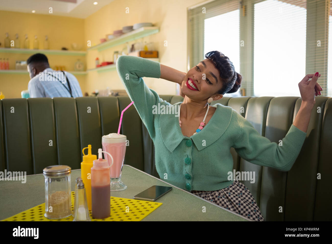 Smiling young woman sitting on couch stretching her arms at restaurent ...