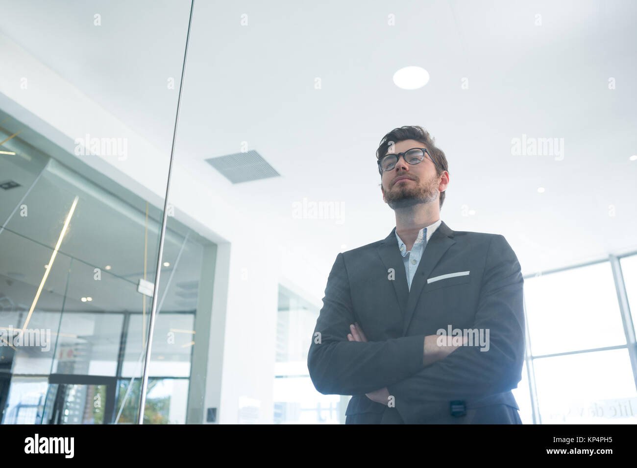 Thoughtful businessman standing with arms crossed in office Stock Photo ...