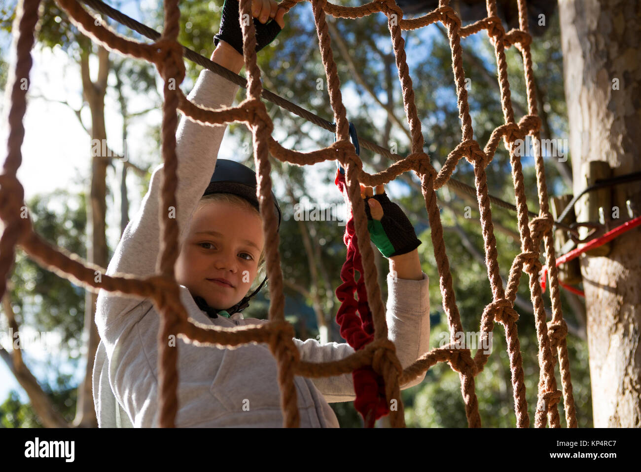 Little girl wearing safety harness climbing rope fence in the forest