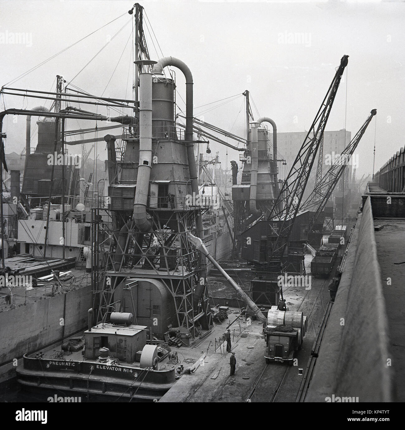1950s, historical picture showing workers and activity with ships and floating pneumatic elevators in dock 9, the King George V Dock ( KGV) the last of the docks to be built and a dock which was able to acomodate large ships, Port of London, England, UK. Stock Photo