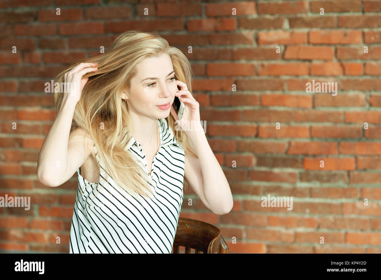 A blonde girl is calling by the phone against a brick wall background, calling the apartment repair service. Advertising of construction services Stock Photo