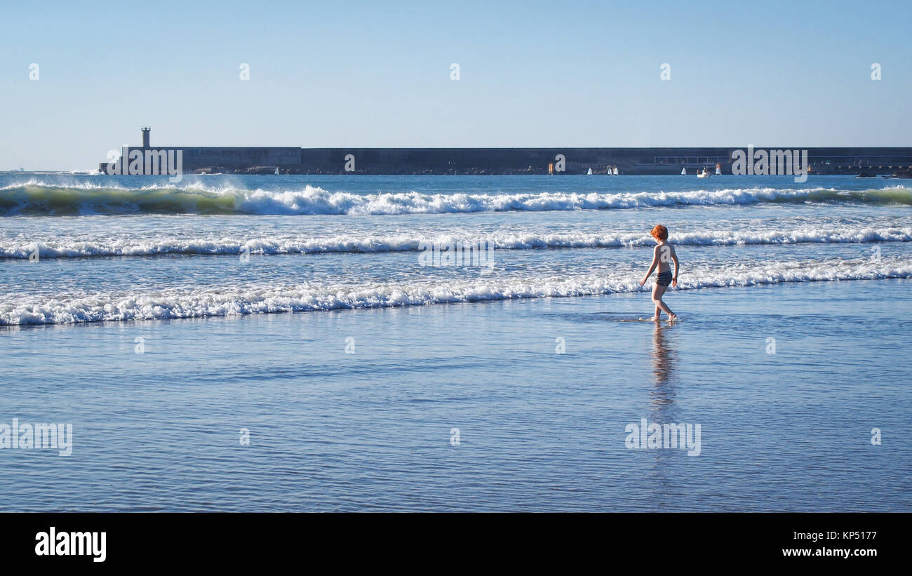 Little red-haired boy enters the Atlantic Ocean surf at Porto, Portugal Stock Photo