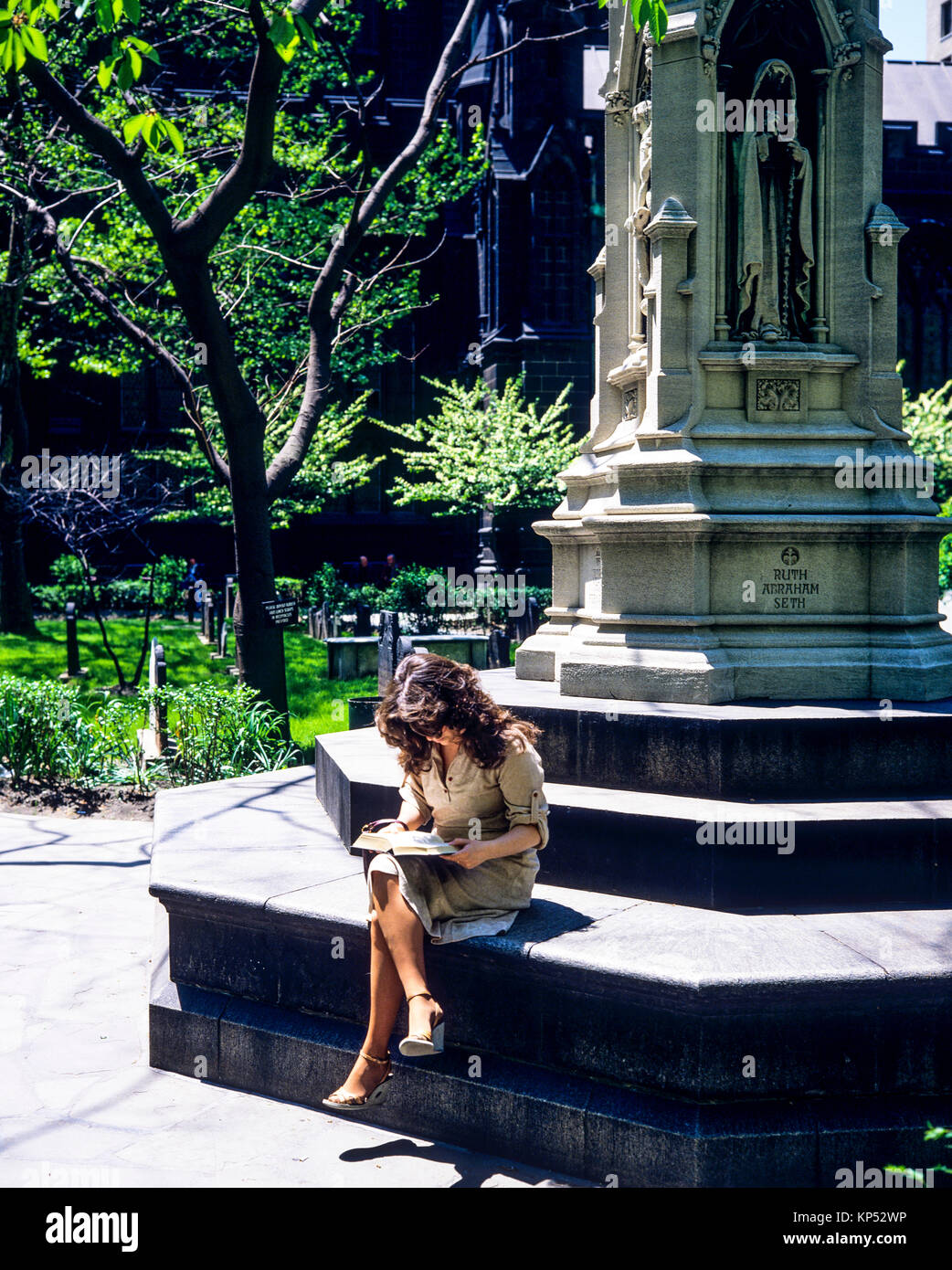 May 1982,New York,woman reading a book,Astor cross,Trinity church cemetery,financial district,lower Manhattan,New york City,NY,NYC,USA, Stock Photo