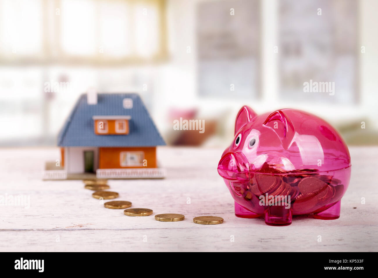 conceptual shot with piggy bank and house scale model on the table in the room Stock Photo