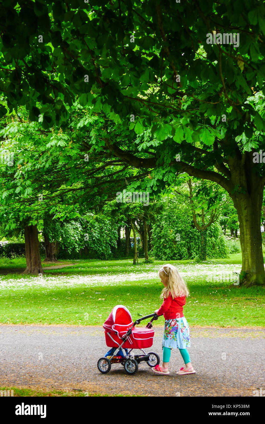 Little girl, child playing with her doll and pram, carriage in the park, children toys, kid toys park Stock Photo