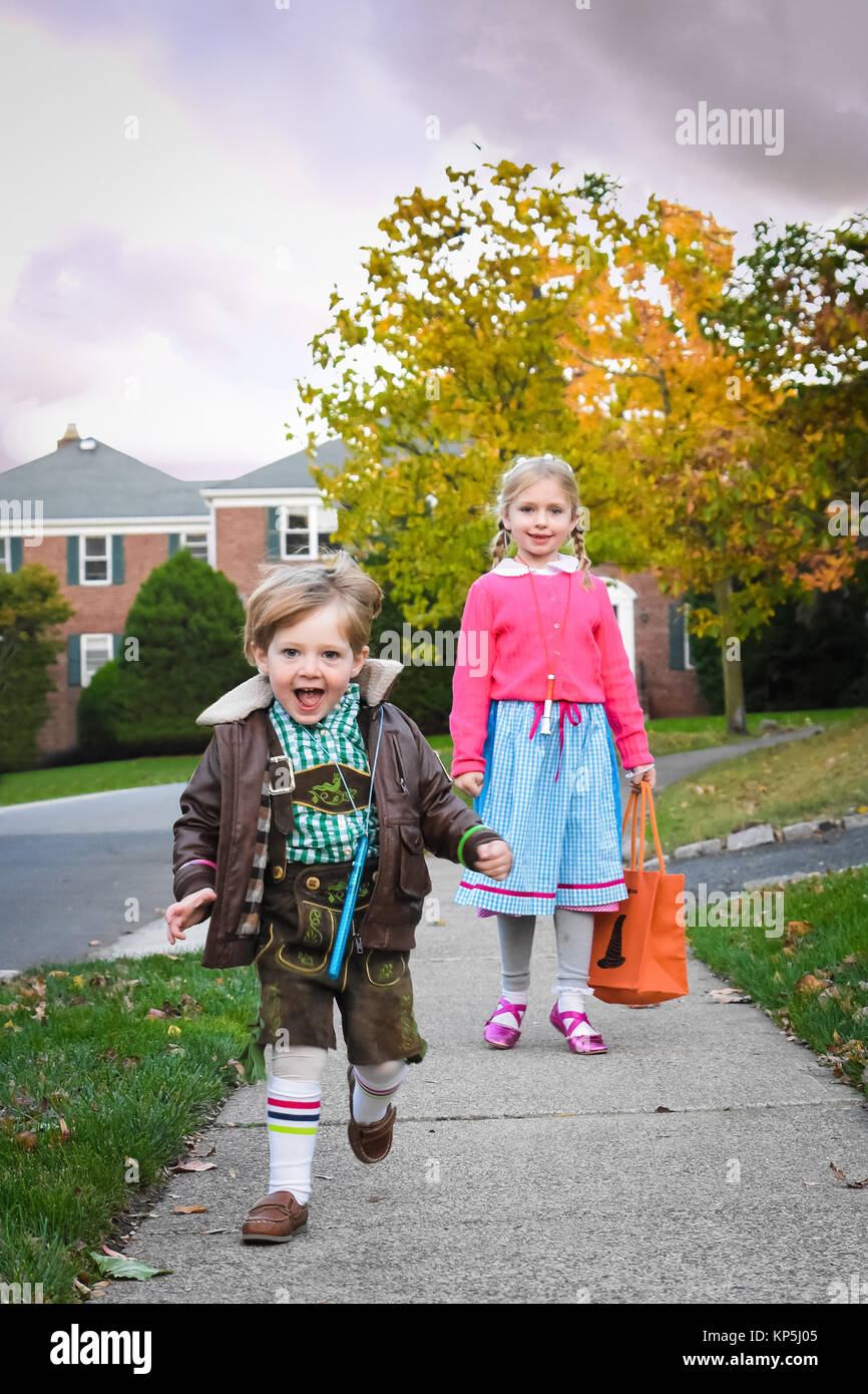 adorable brother and sister siblings walking down street to go Trick or Treating on Halloween Stock Photo