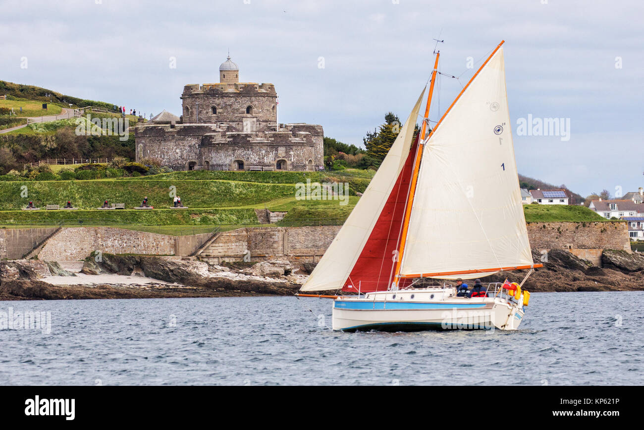 Small yacht with red and white sails passing St Mawes Castle on the Roseland peninsula in Cornwall UK Stock Photo