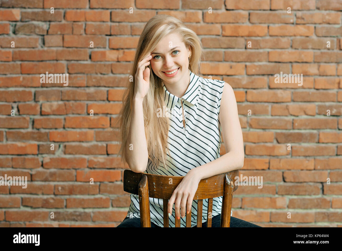 A blonde girl is calling by the phone against a brick wall background, calling the apartment repair service. Advertising of construction services Stock Photo