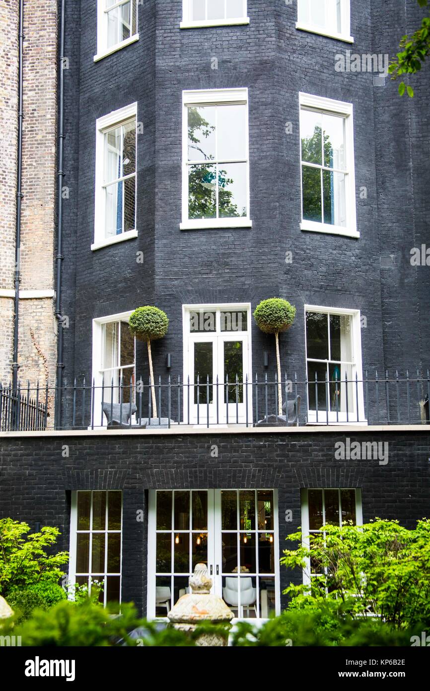 Very tall and modern dark grey town house with many windows and adorned with french doors and many greens in the garden