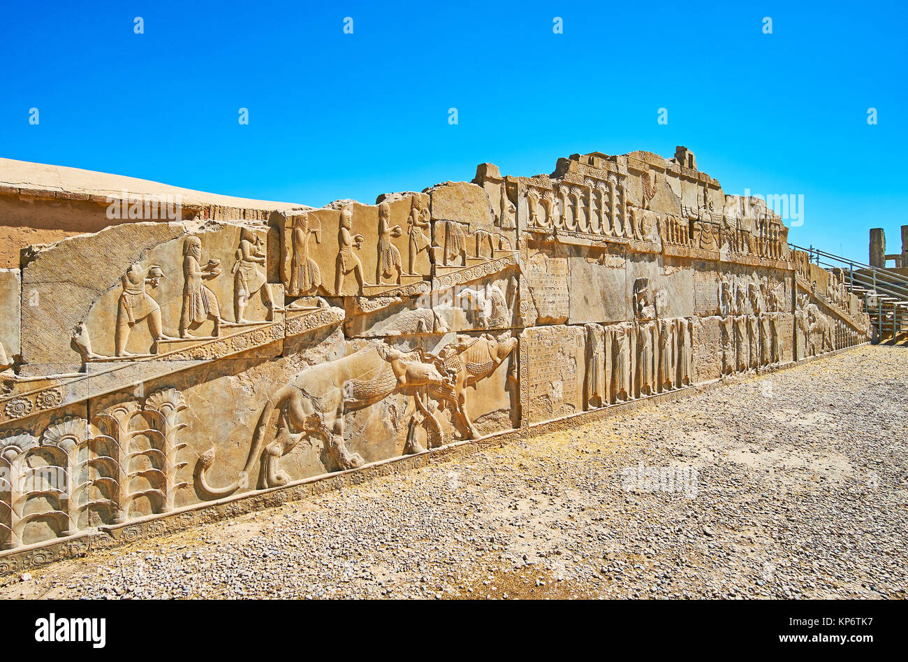 The ruined facade wall of the ancient palace of Xerxes (Hadish) with preserved reliefs, including classical Persian themes - lion and bull, soldiers a Stock Photo