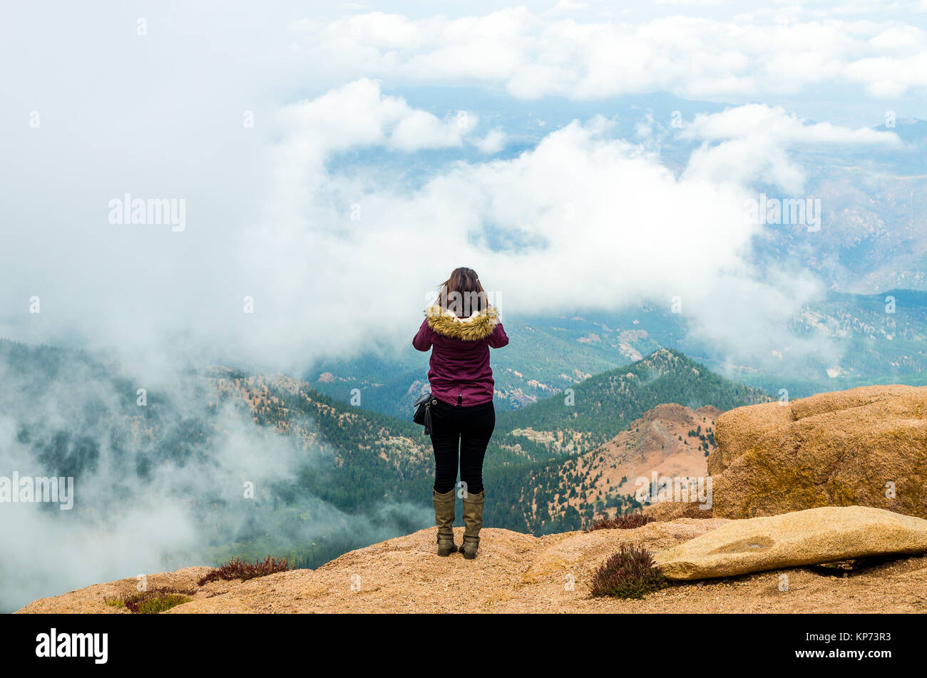 Girl enjoying the beauty of rocky mountain in pike peak Colorado and watching from the mountain on an unusual seascape with clouds over the sea s Stock Photo