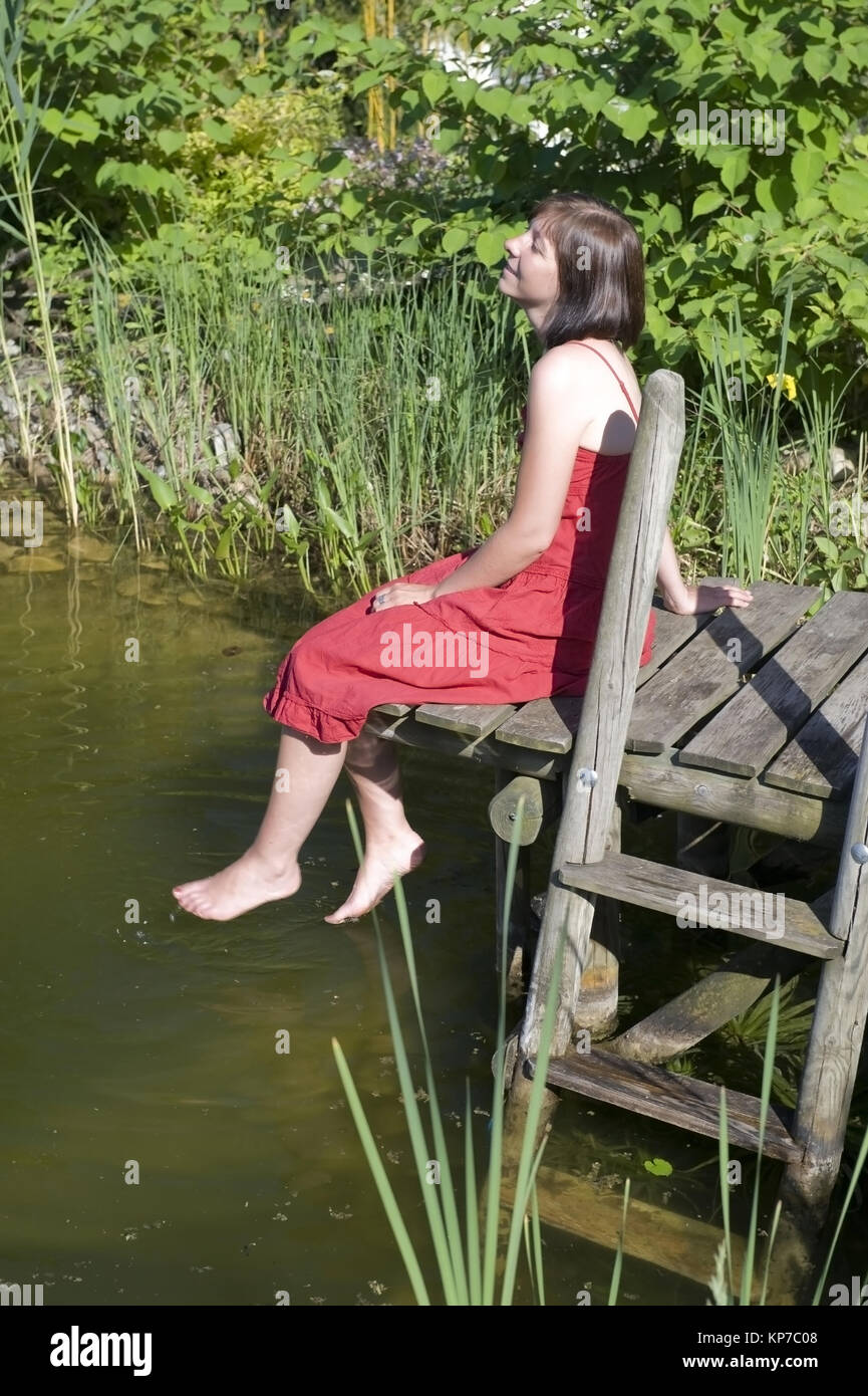 Model release, Junge Frau im roten Kleid sitzt auf Steg am Teich