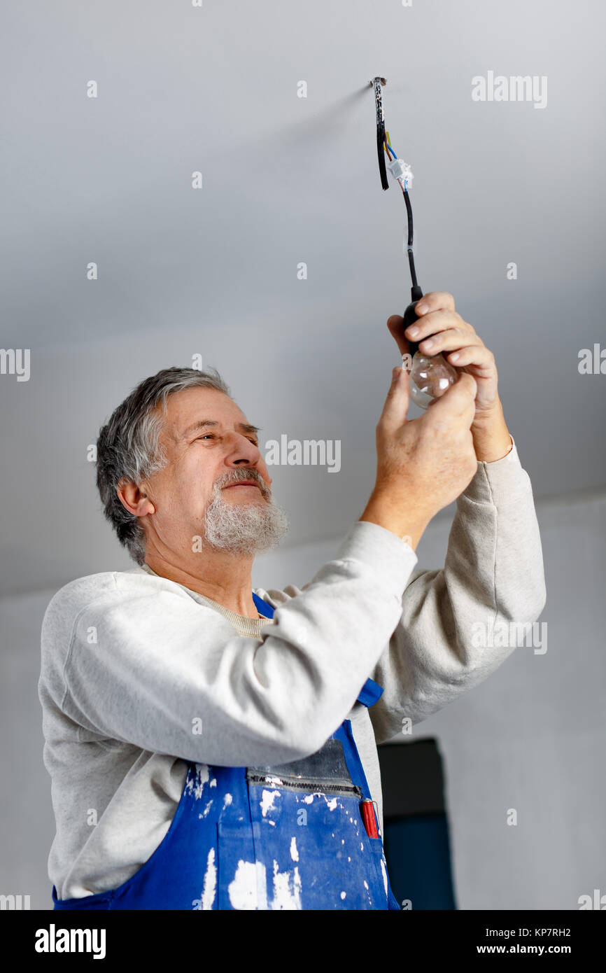 Senior man installing a ceiling light in a freshly renovated appartment Stock Photo