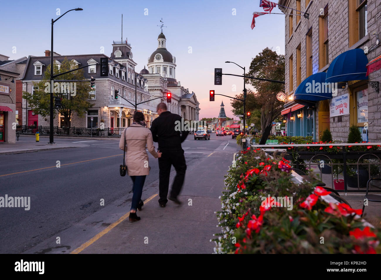 A tourist couple passing by historical buildings along Ontario Street with Kingston City Hall in the distance in downtown Kingston, Ontario, Canada. Stock Photo