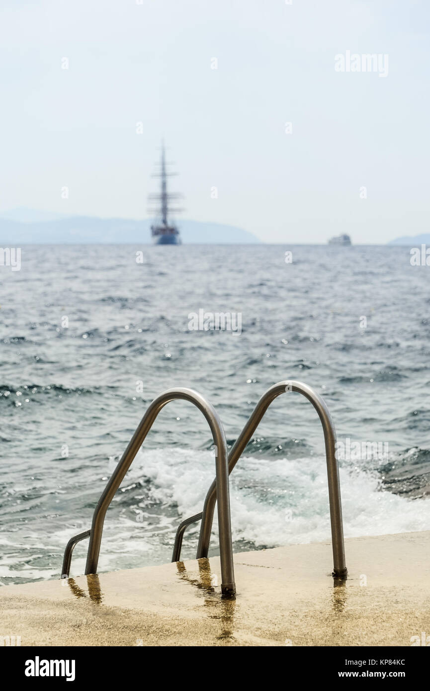 swim ladder on the rocky beach behind a sailing ship Stock Photo