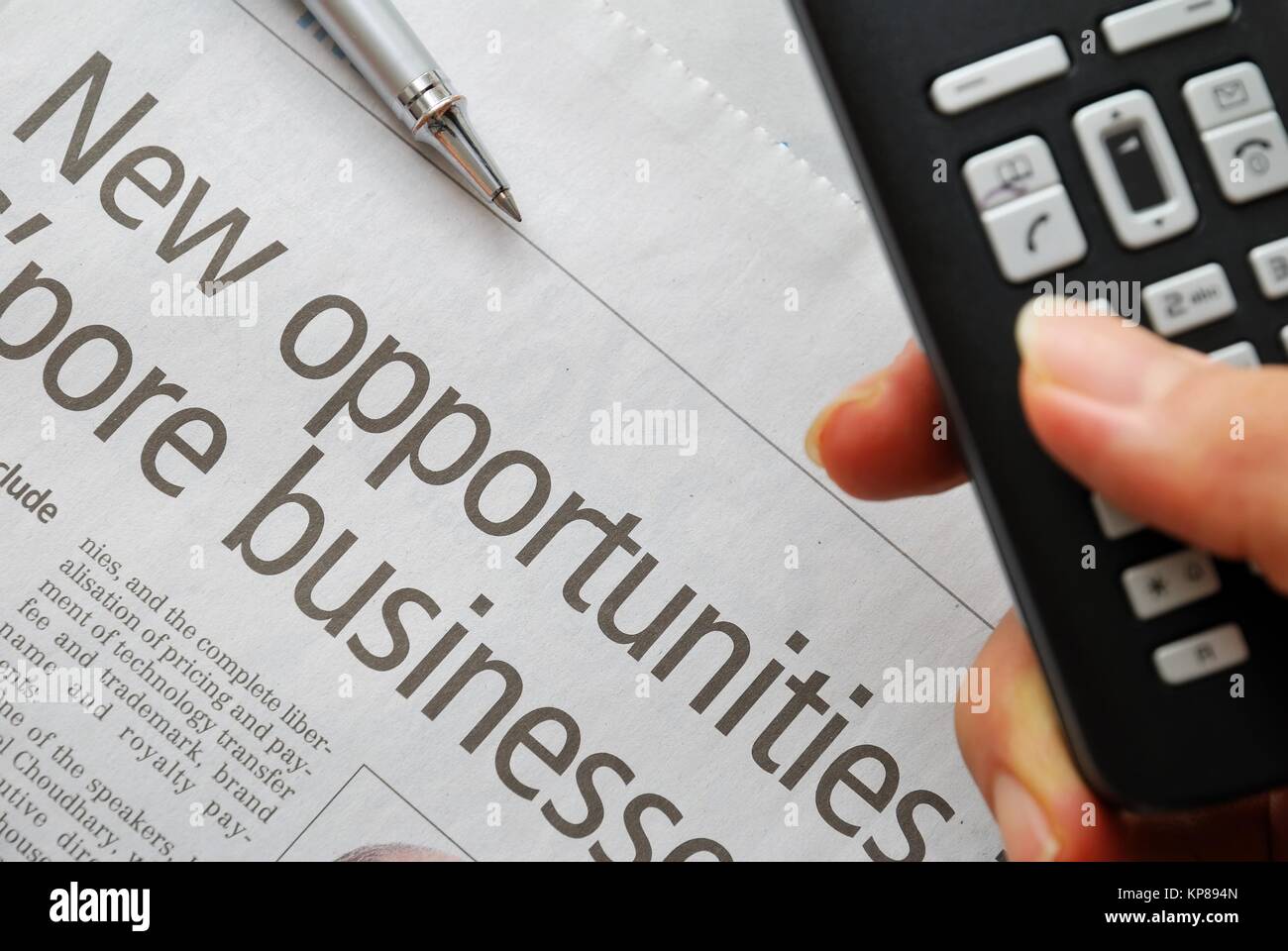 Closeup of new opportunities text on newspaper with hand dialing phone in foreground, signifying business and success, office life and job searching c Stock Photo