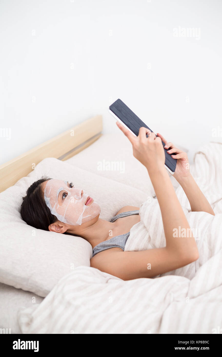 Woman lying down with using facial mask adn tablet pc Stock Photo