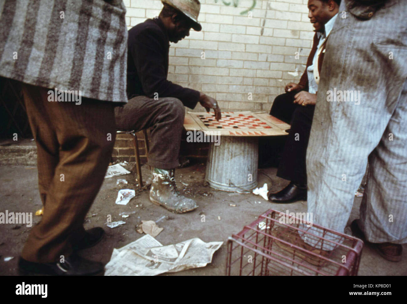Hard working man on left playing checkers with friends before returning to work. Stock Photo