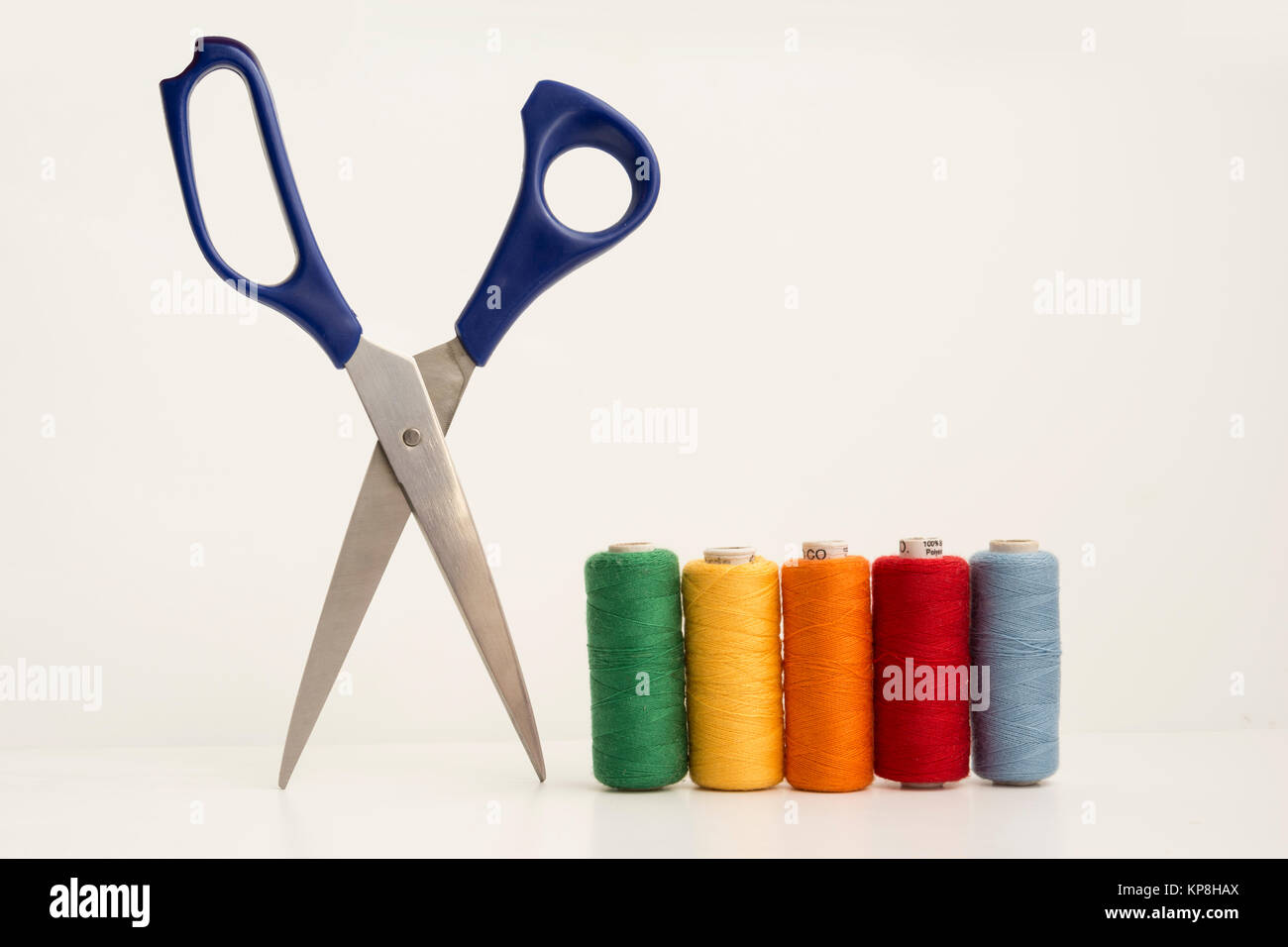 Sewing accessories and tools. Red sewing threads, black scissors, yellow  measuring tape and thimble on a white background. Stock Photo