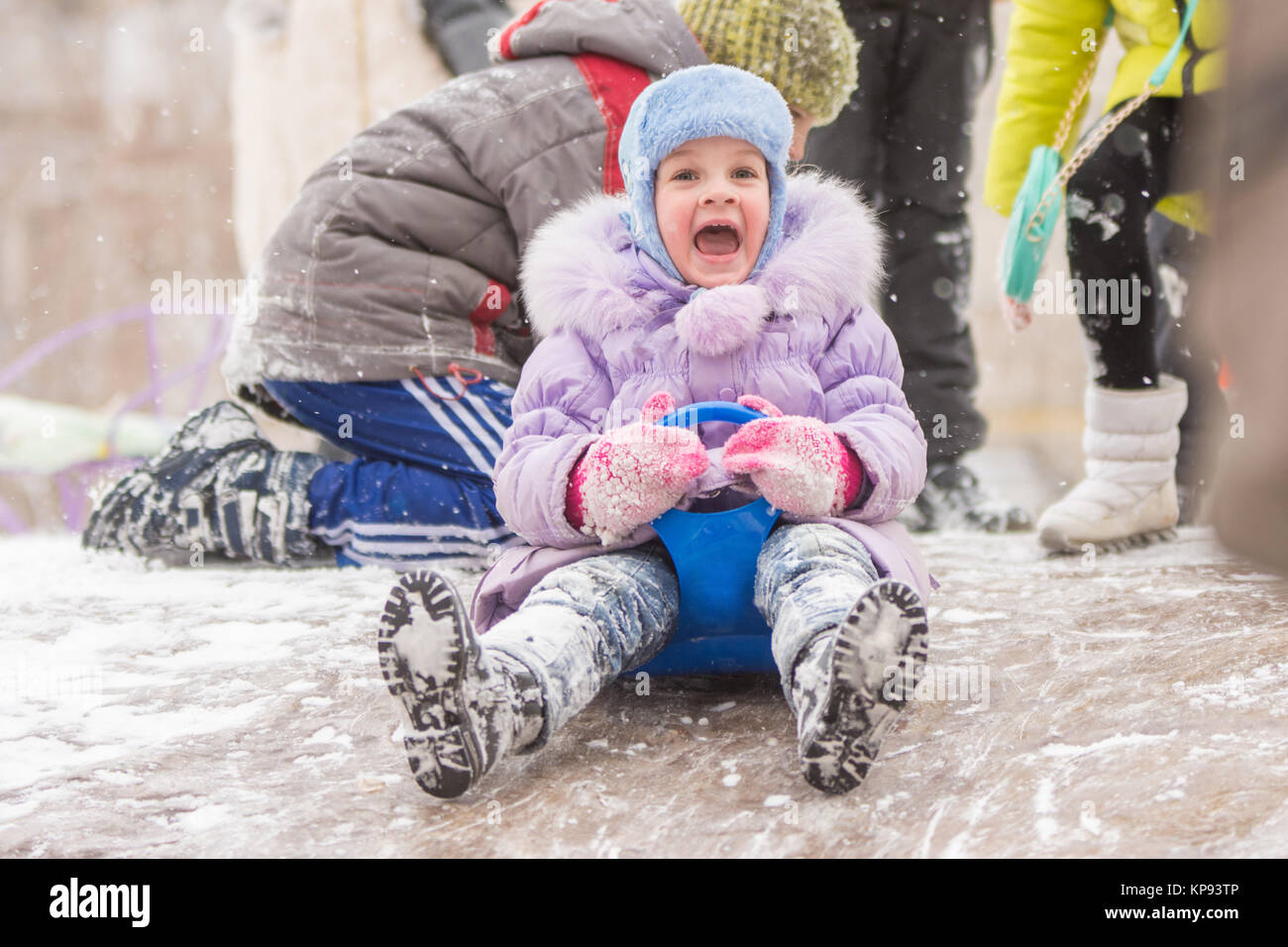 Five-year girl fun screaming slides down the icy hill Stock Photo