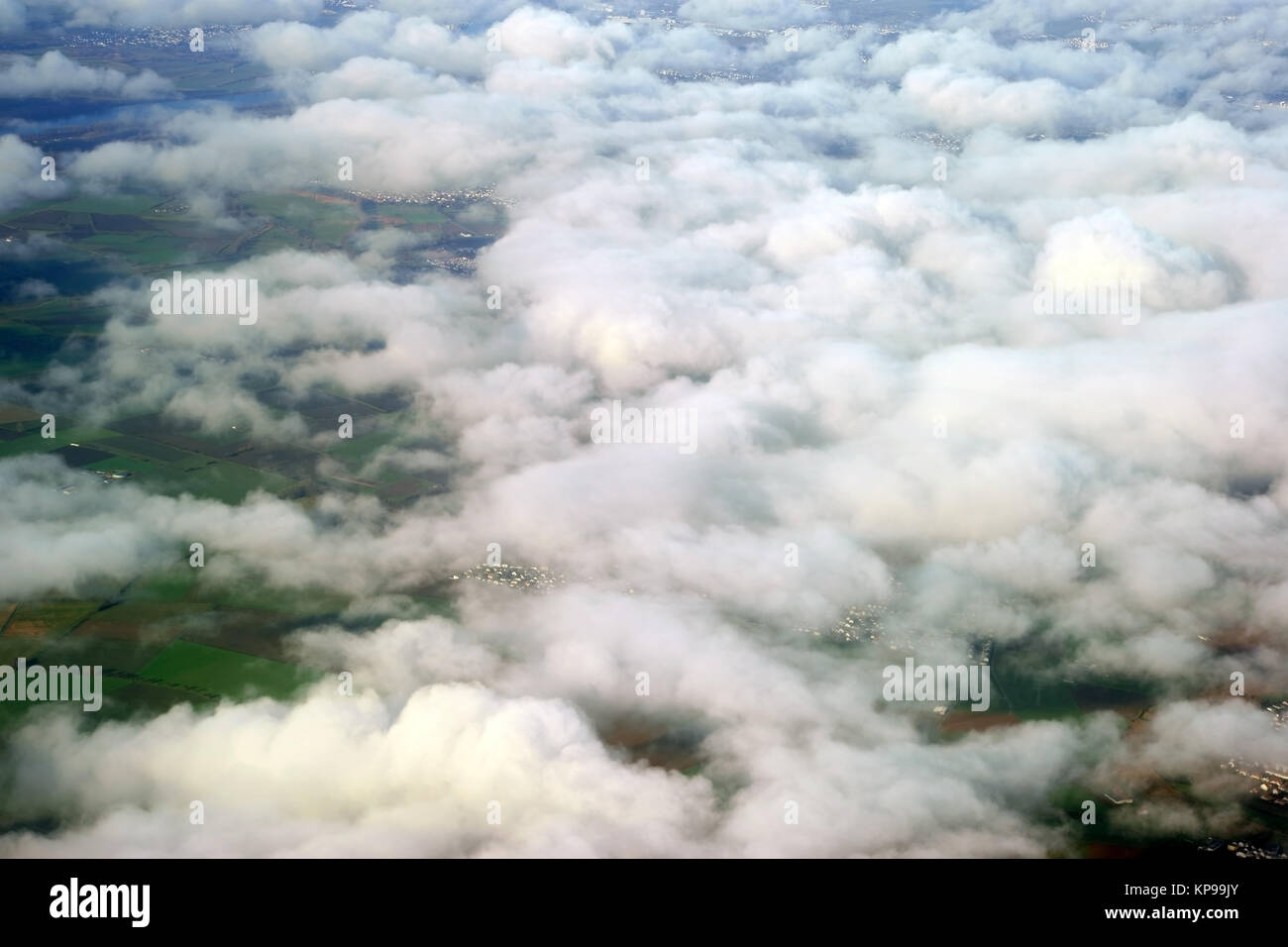 Wolkenaufnahmen aus dem Flugzeug heraus mit darunterliegenden Wiesen und Feldern. Stock Photo