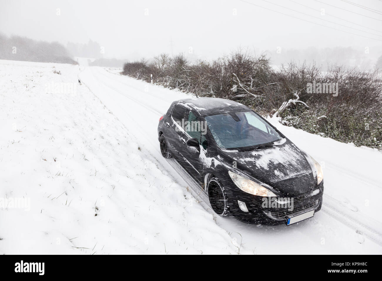 Black car on a snow covered road in a snowy white winter landscape Stock Photo